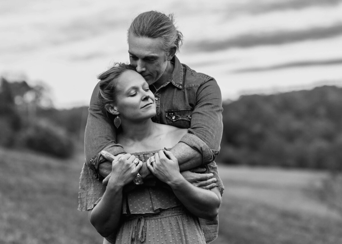 A black and white photo of a couple embracing in a field, captured by a Pittsburgh family photographer.