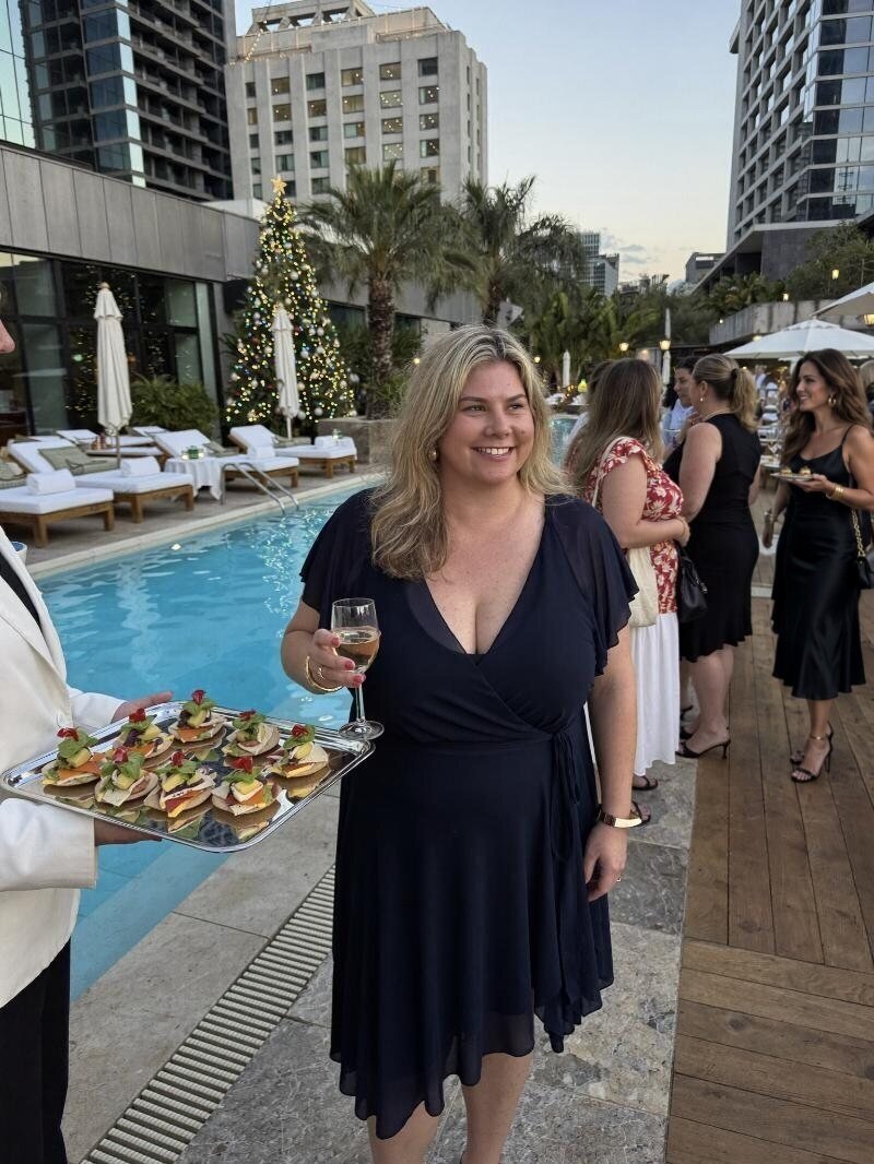 Renee holding champagne by a hotel pool as a waiter offers canapés