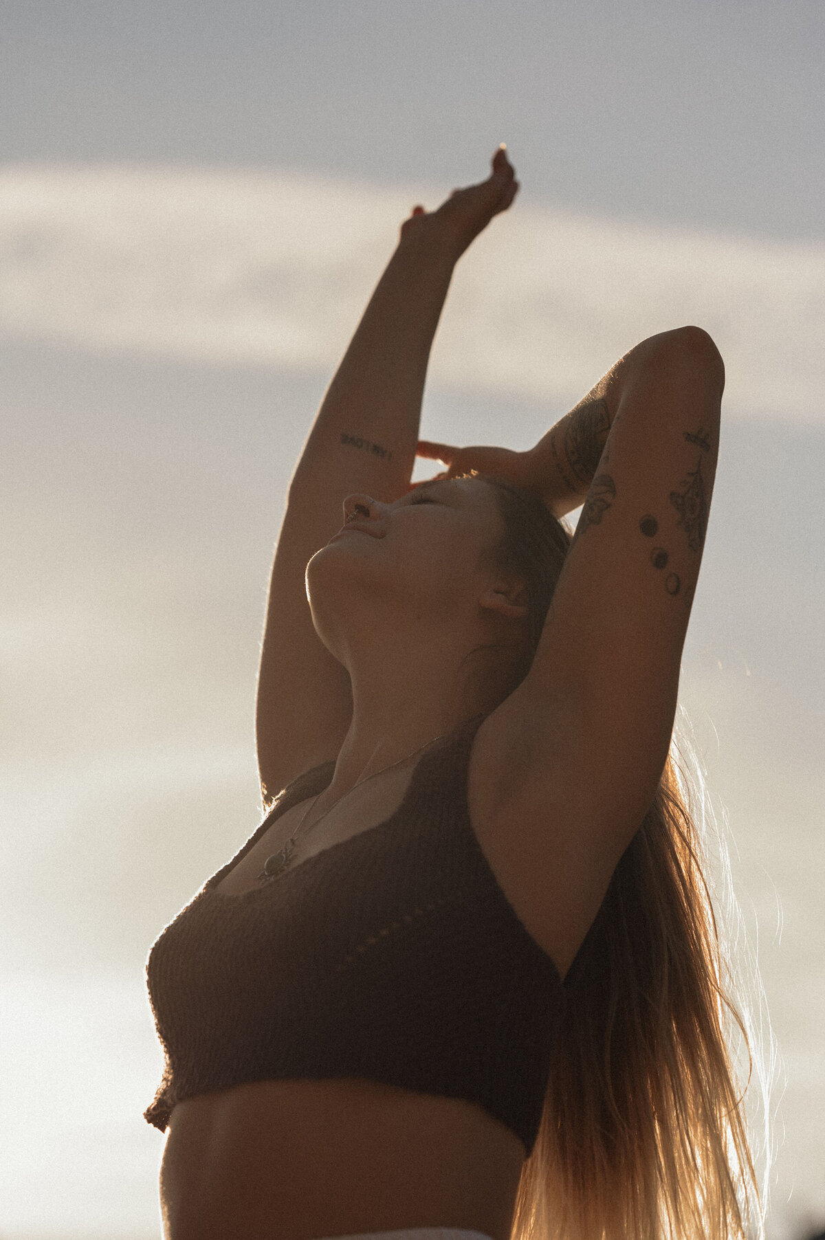 natural woman embraces her beauty as she poses and stands against a sunset backdrop