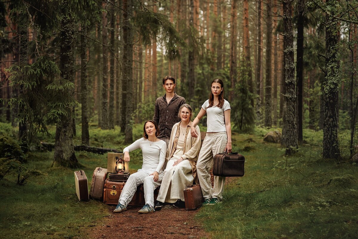 Familjefoto i skogen. kvinna och hennes tre barn som är unga vuxna. De är omgivna av resväskor.