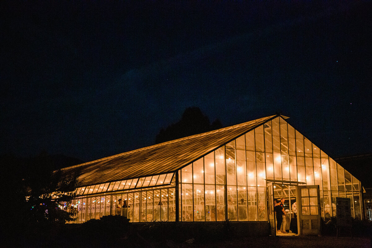 A view of the greenhouse lit up at night under the night sky at Dos Pueblos Orchid Farm in Santa Barbara by film photographer Megan Lynn of My Sun and Stars Co.