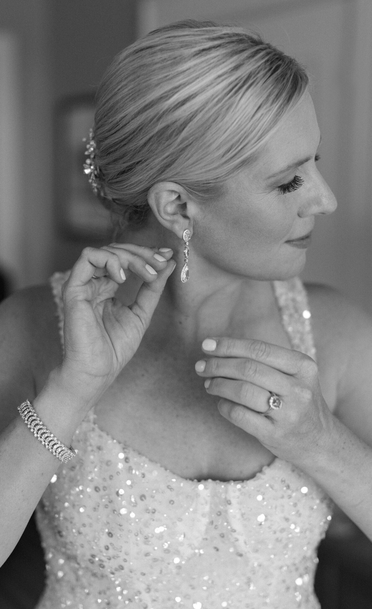 Bride adjusts earring while wearing a sparkly wedding dress.