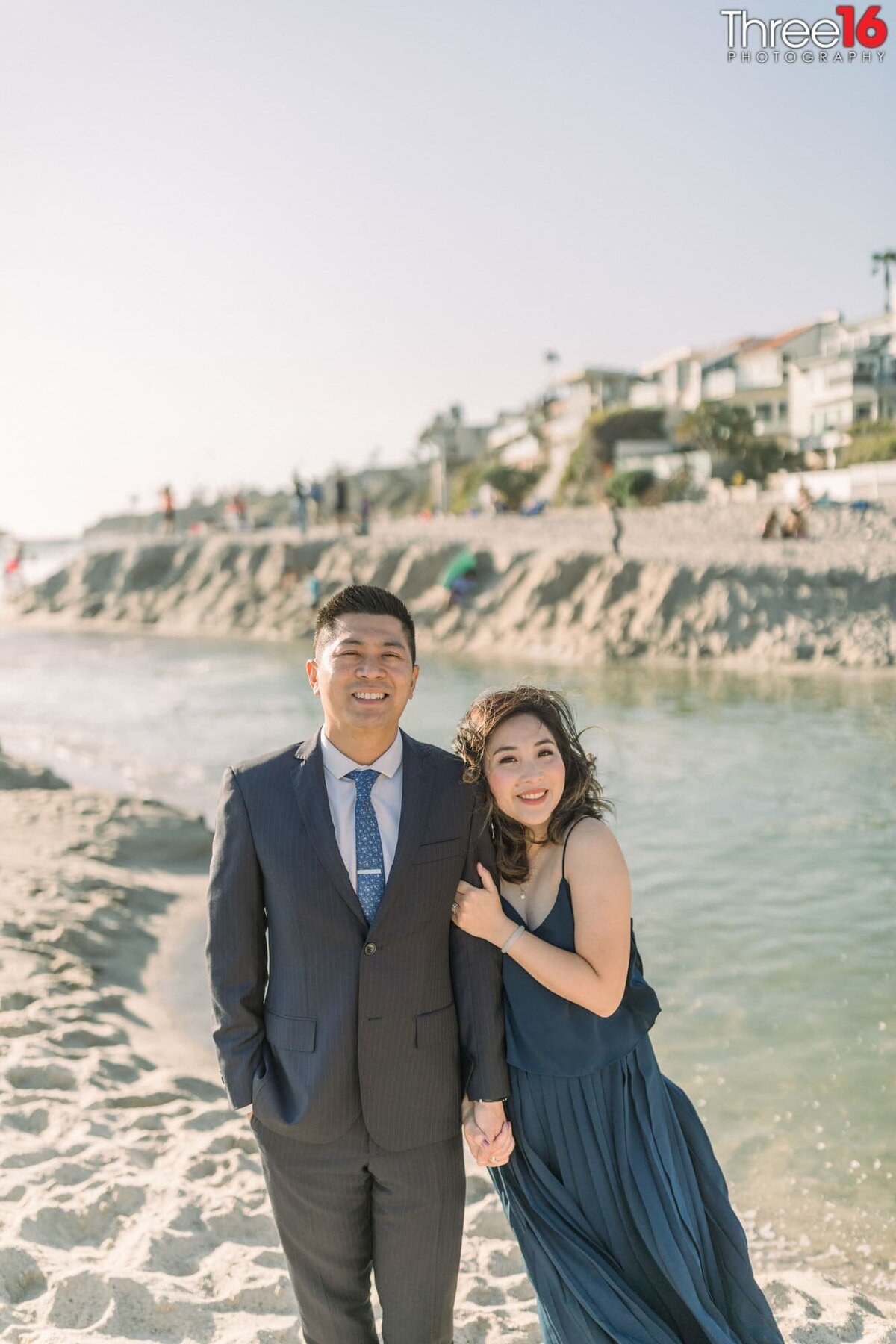 Bride to be leans up against her fiance on sands of Aliso Beach