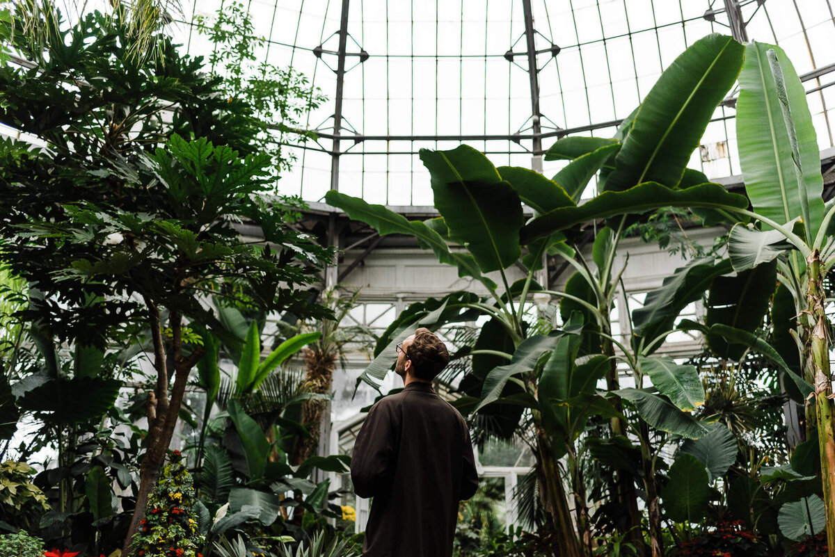 Man standing in atrium, surrounded by tropical plants.