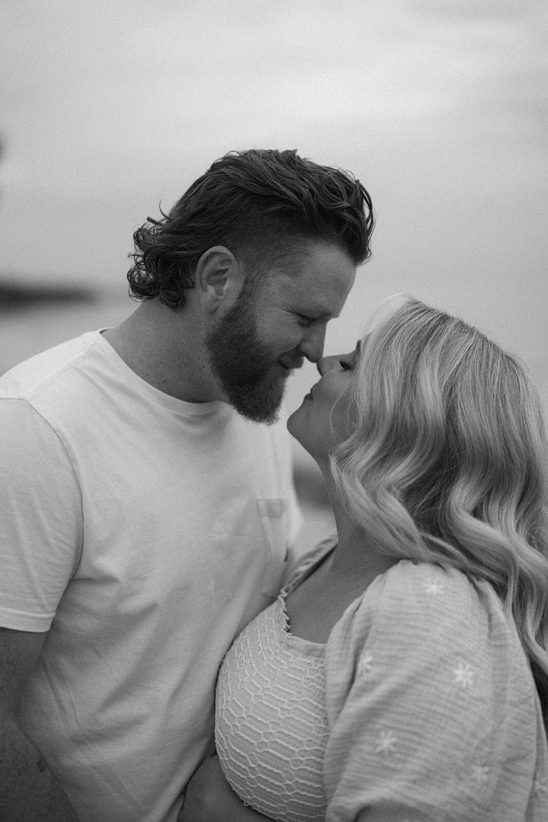 Pregnant couple sharing an intimate moment at South Haven North Beach with soft sunset light behind them.