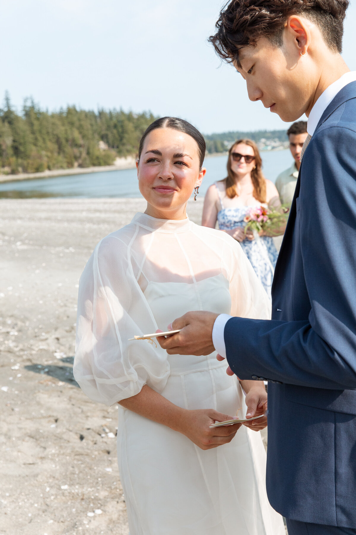 Bride looks towards the officiant while groom look at his vows during beach wedding