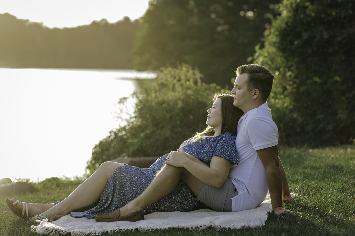 Verona B Photography captures a beautiful maternity picture of an expectant couple enjoying being together and looking peacefully at the water at Silver Creek Metro Park in Norton, OH while the sun starts to dip below the horizon. There is so much peace and serenity in this beautiful lake setting near Akron, OH.