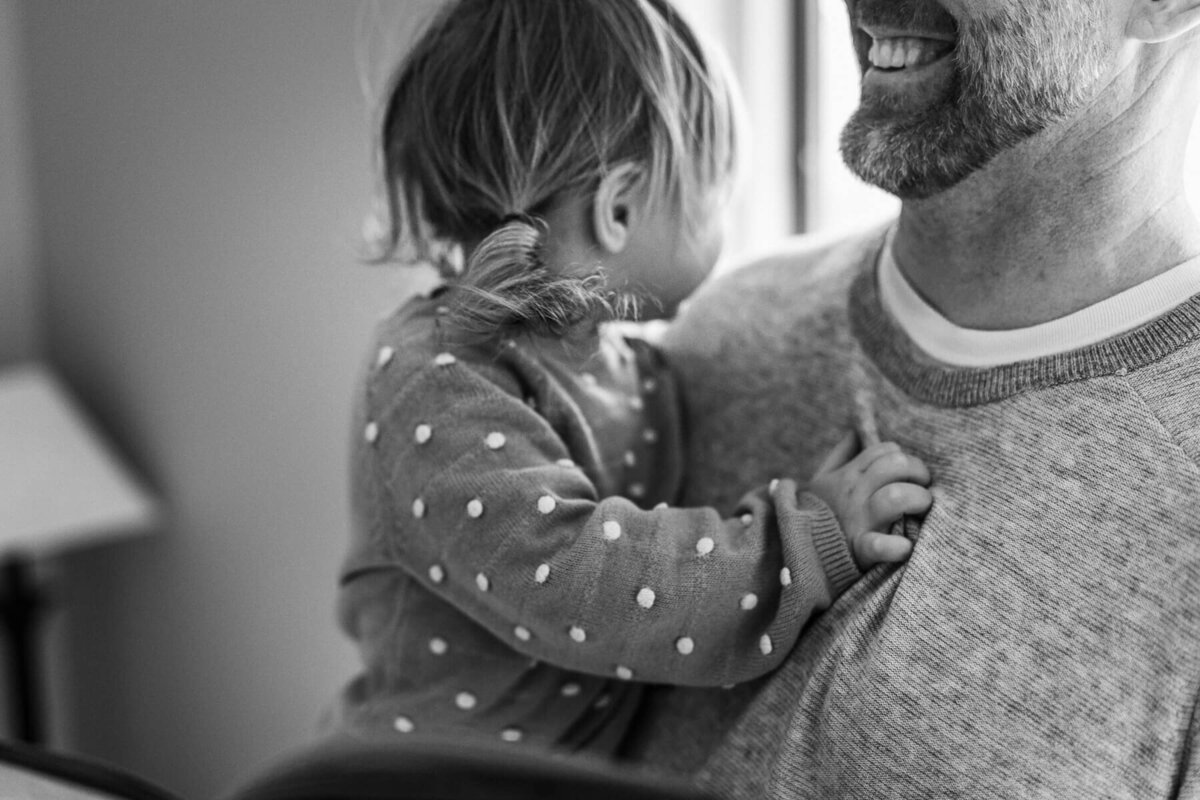 A black and white image that is a close up of a small girls pig tail curls while being held by her father.