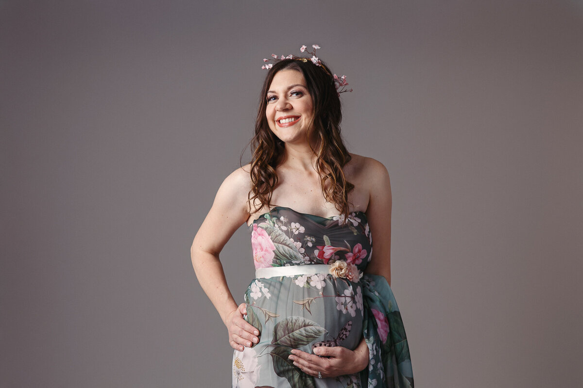 Close up portrait of pregnant woman wearing a green floral gown photographed on a grey background