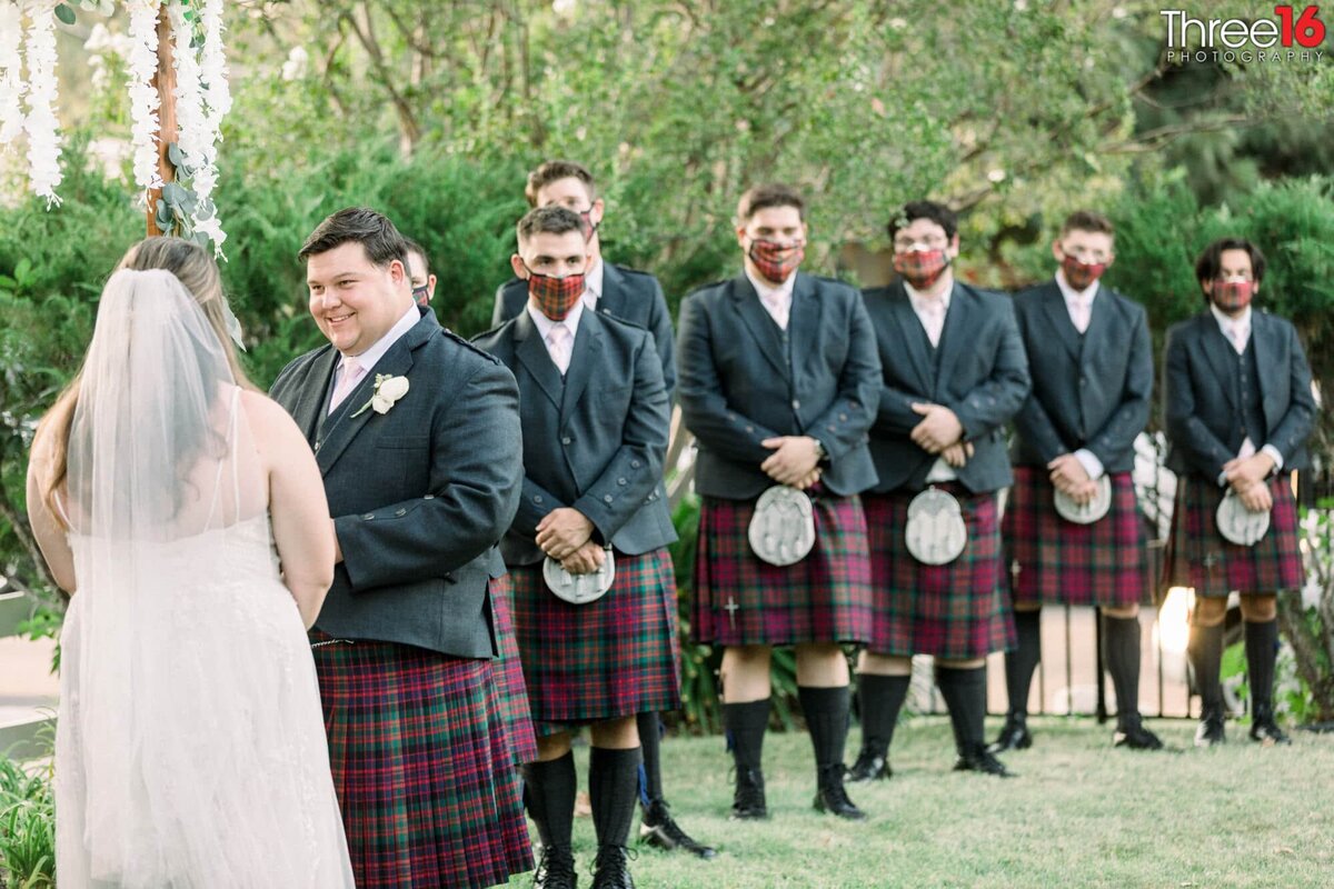 Groomsmen stand by in kilts and masks watching the Bride and Groom get married
