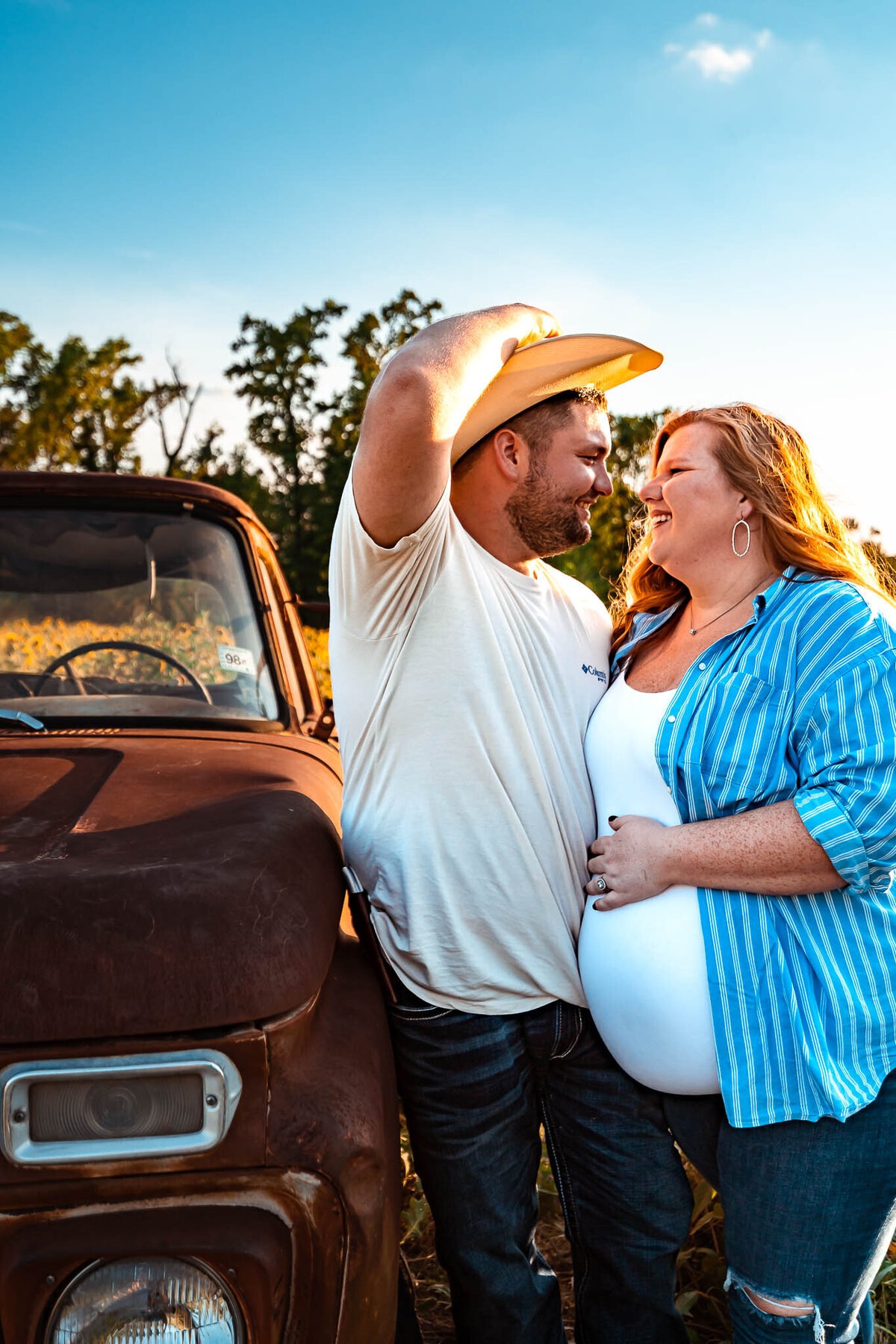 Couple smiling in a field of sunflowers in longview texas wearing a t-shirt and jeans leaning on an old truck