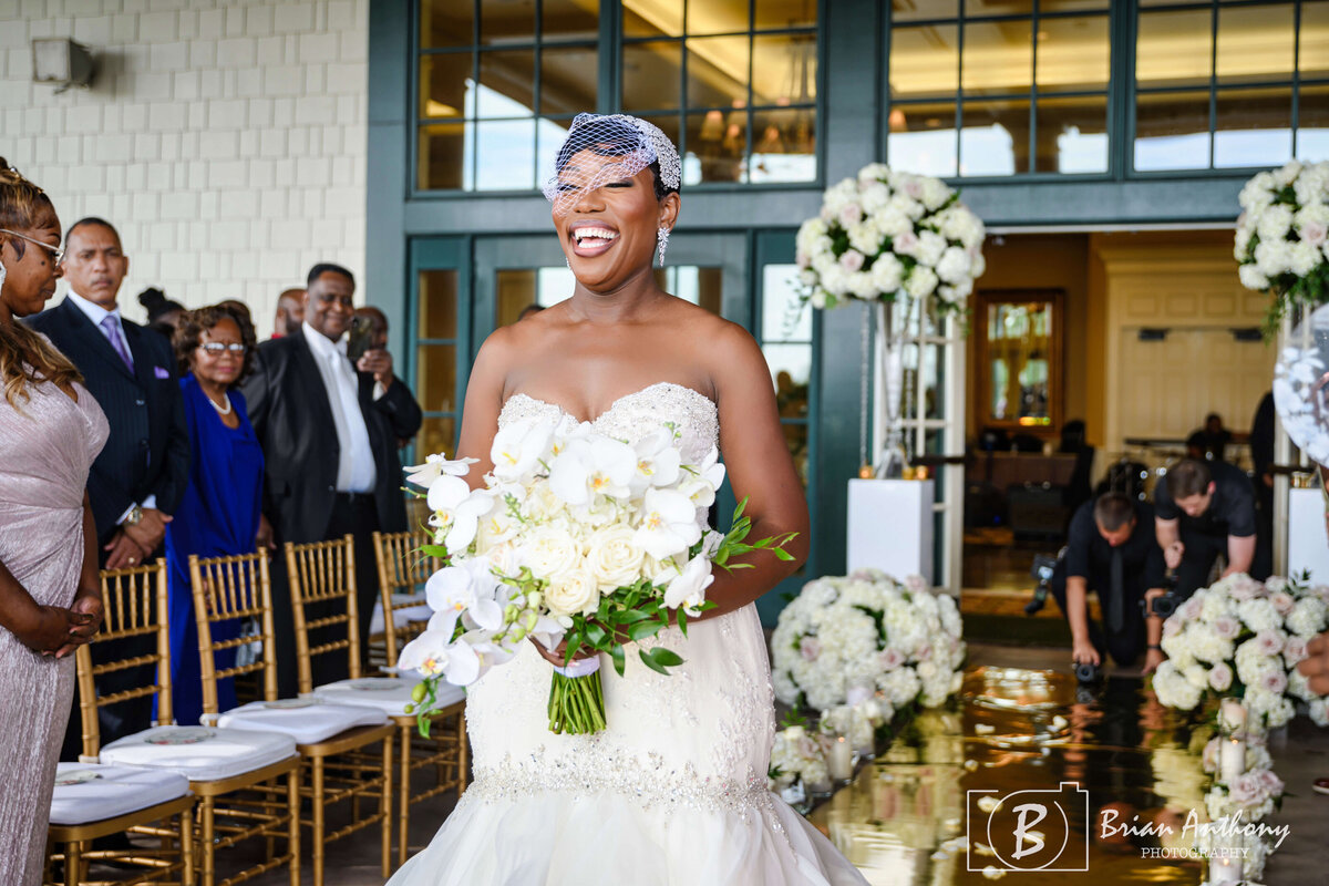 Radiant bride walking down the aisle with a bouquet of white roses and greenery.