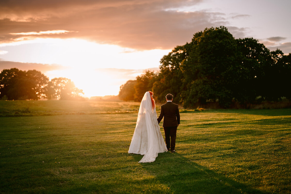 couple walking in golden hour towards the horizon with veil behind