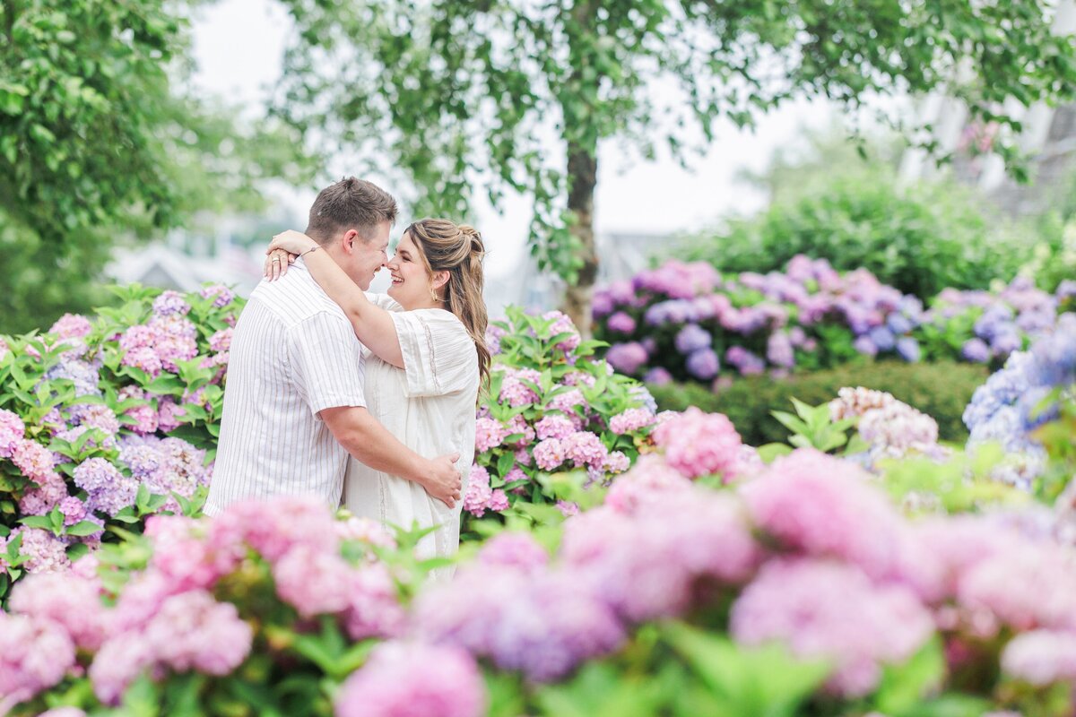Couple standing closely in a garden of blooming hydrangeas, smiling warmly at each other, taken at Chatham Bars Inn in Chatham, Massachusetts — representing the portfolio of a Cape Cod engagement photographer.