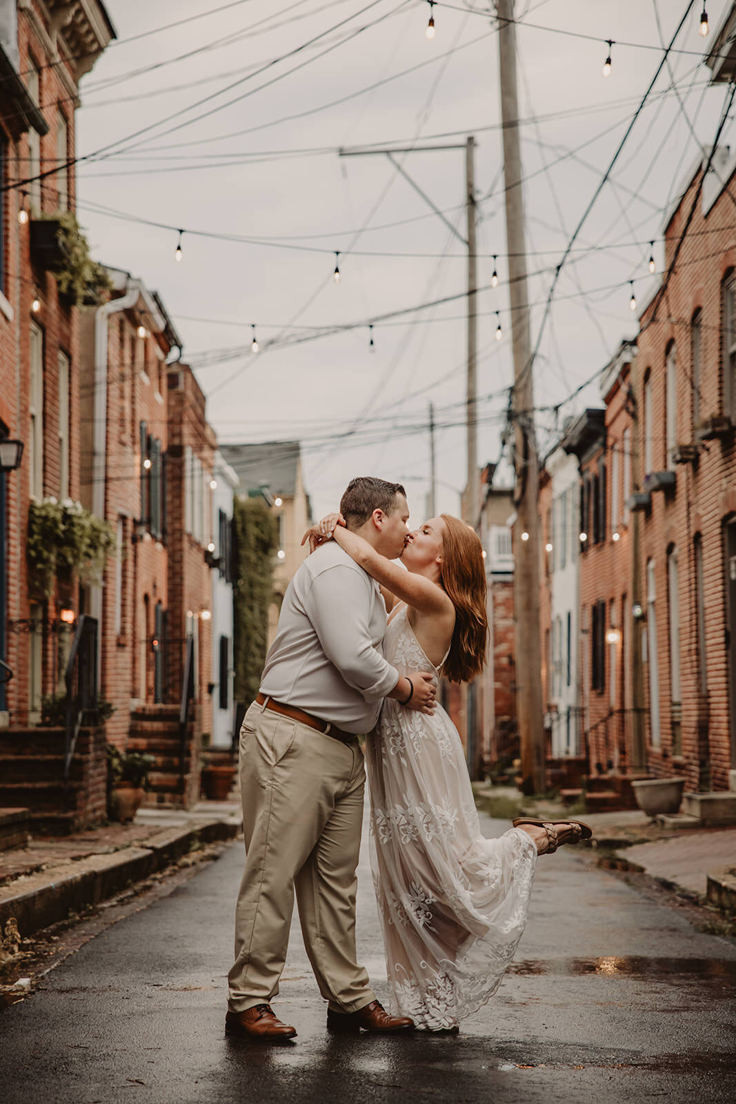 A couple kissing in an alley with string lights overhead 