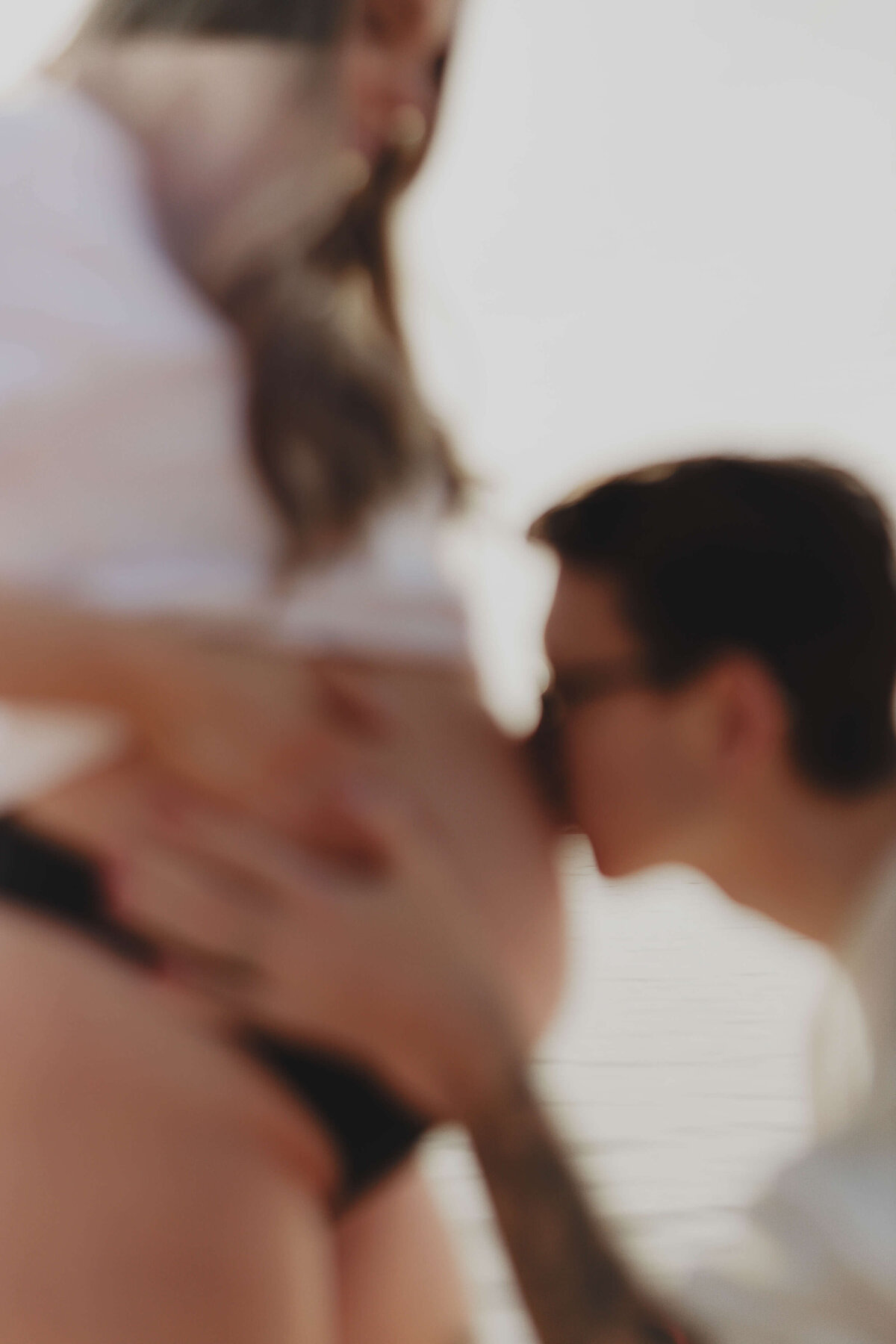 En närbild på en gravid kvinna och hennes partner som pussar hennes gravida mage under en fotografering i Stockholm