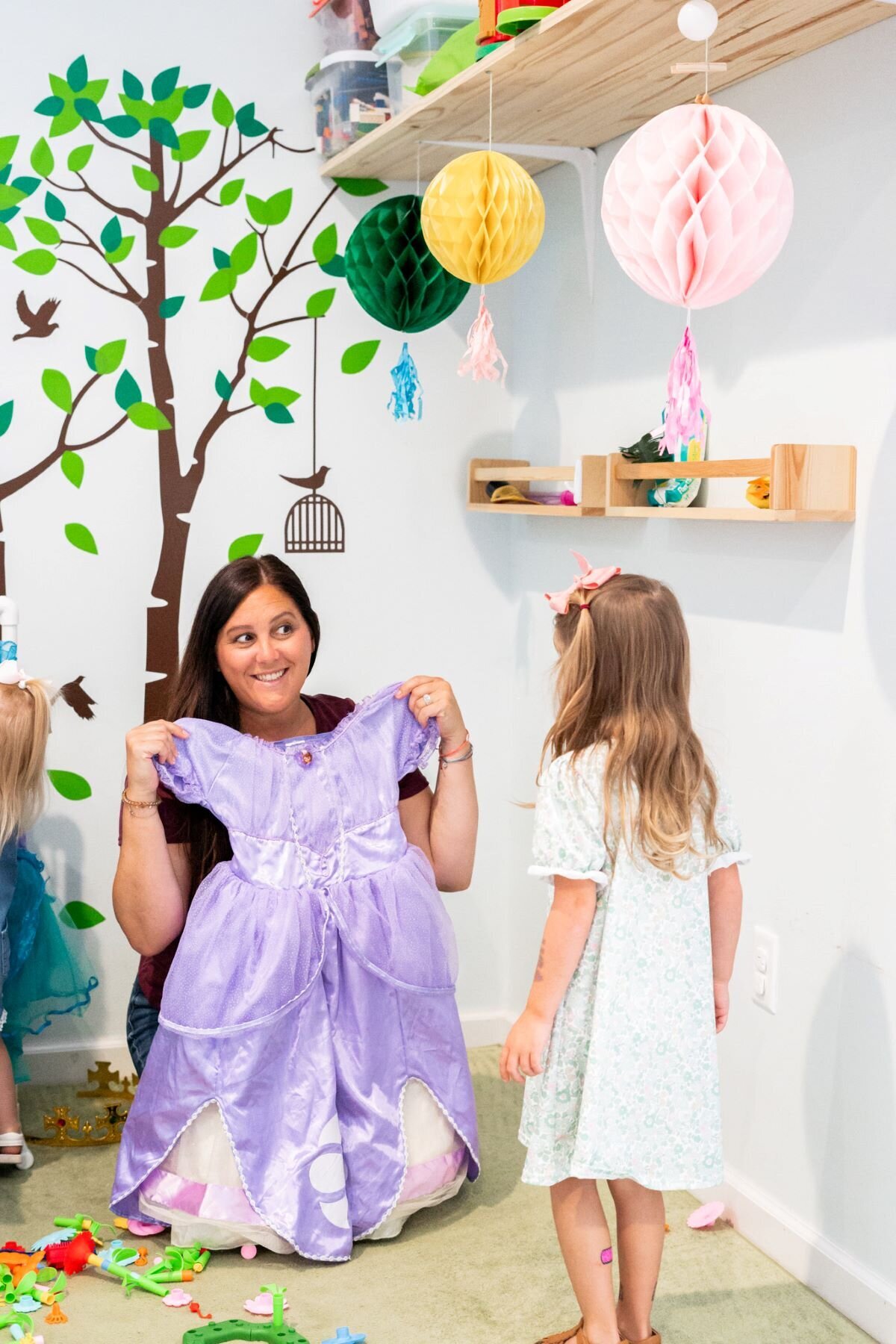 Ms. Brandi holding up a purple princess dress for a young student in the classroom at The Nest, a preschool and learning center in Surf City, North Carolina