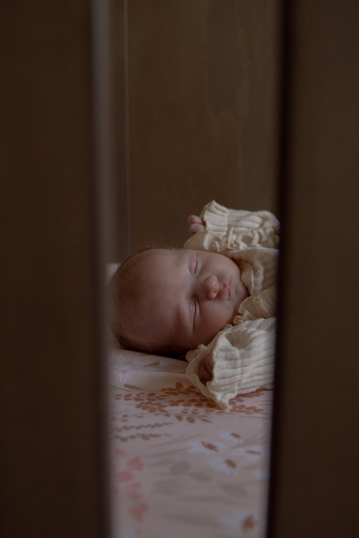 close up of baby's face looking through the crib while baby sleeps on pink floral sheets