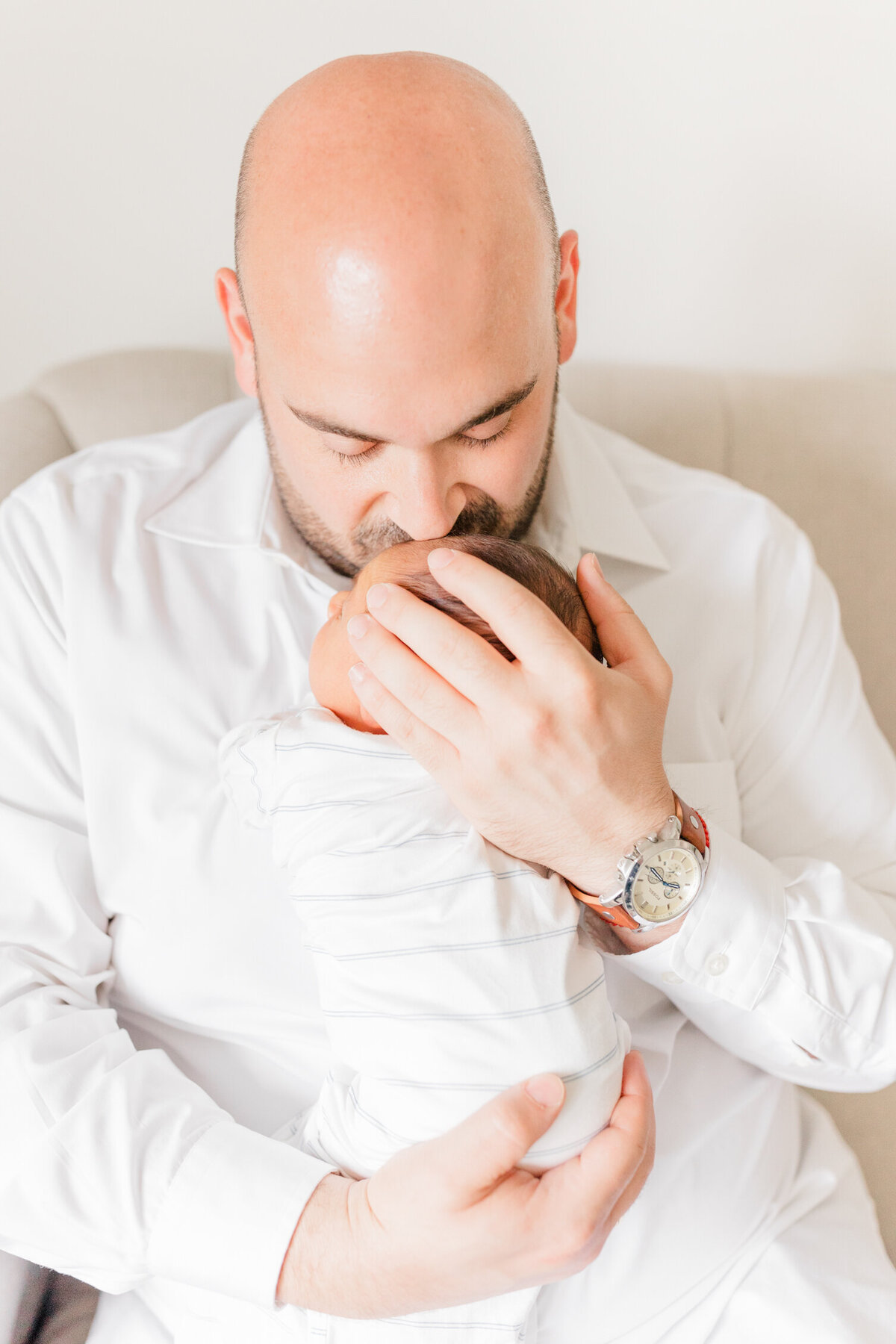 Bald father hugging his newborn to his chest and kissing his head