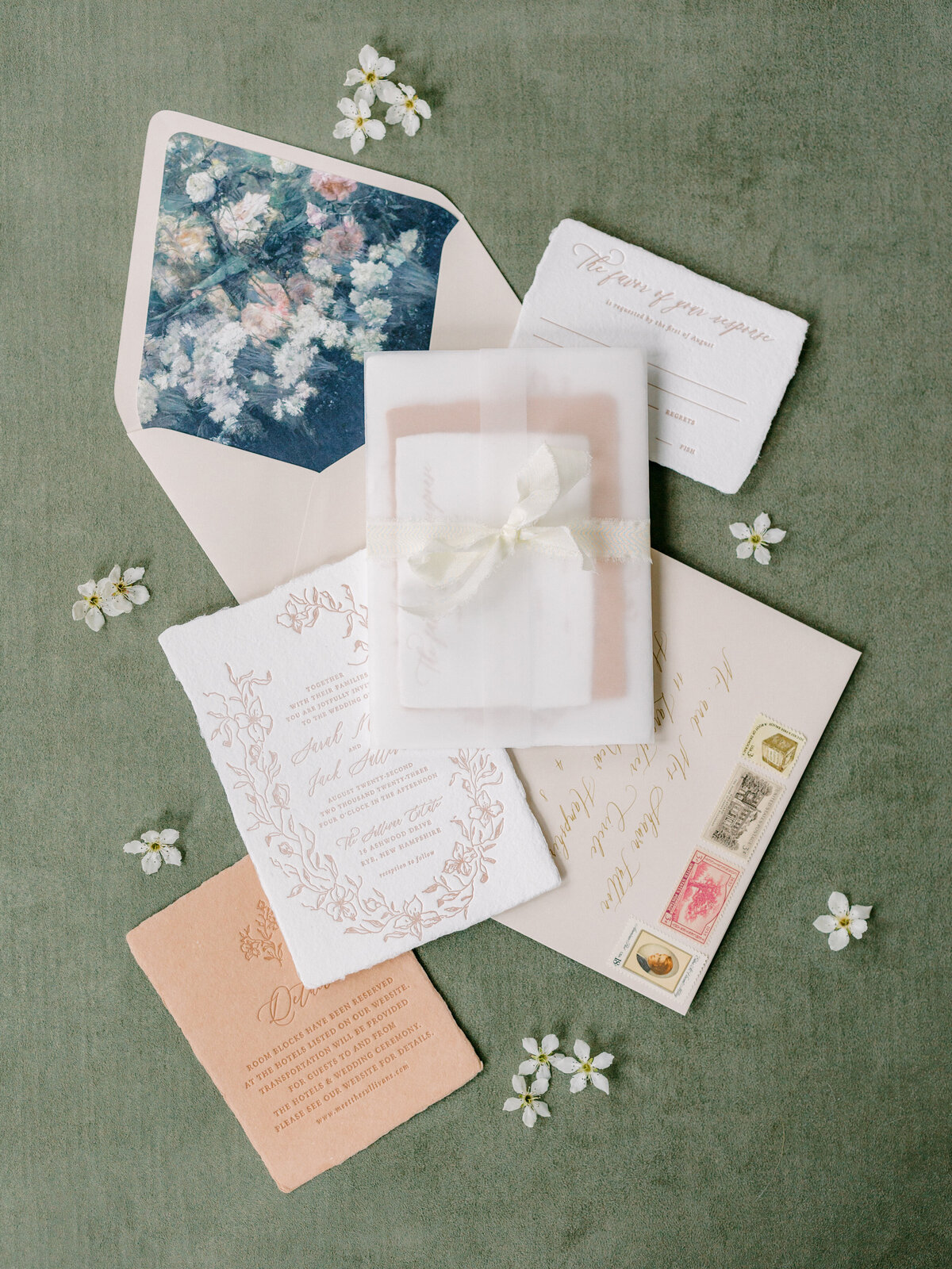 Cream and peach wedding invitation suite with white flowers on a green background