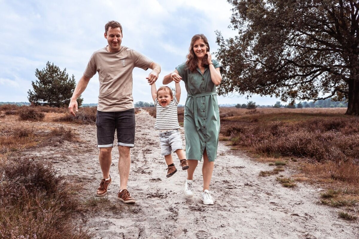 Een gelukkig gezin geniet van een wandeling in de natuur, waarbij de ouders hun kind vasthouden en laten 'vliegen