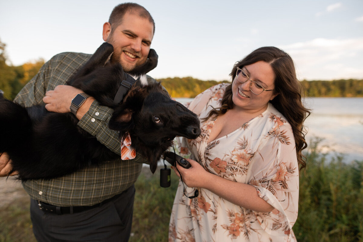 Engaged couple holds their puppy while smiling