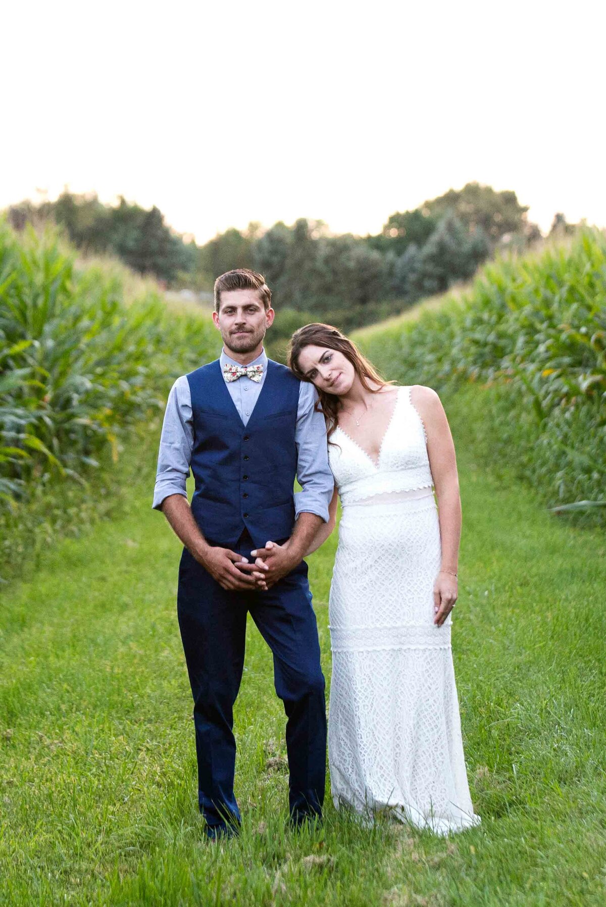 bride and groom standing, holding hands in a corn field