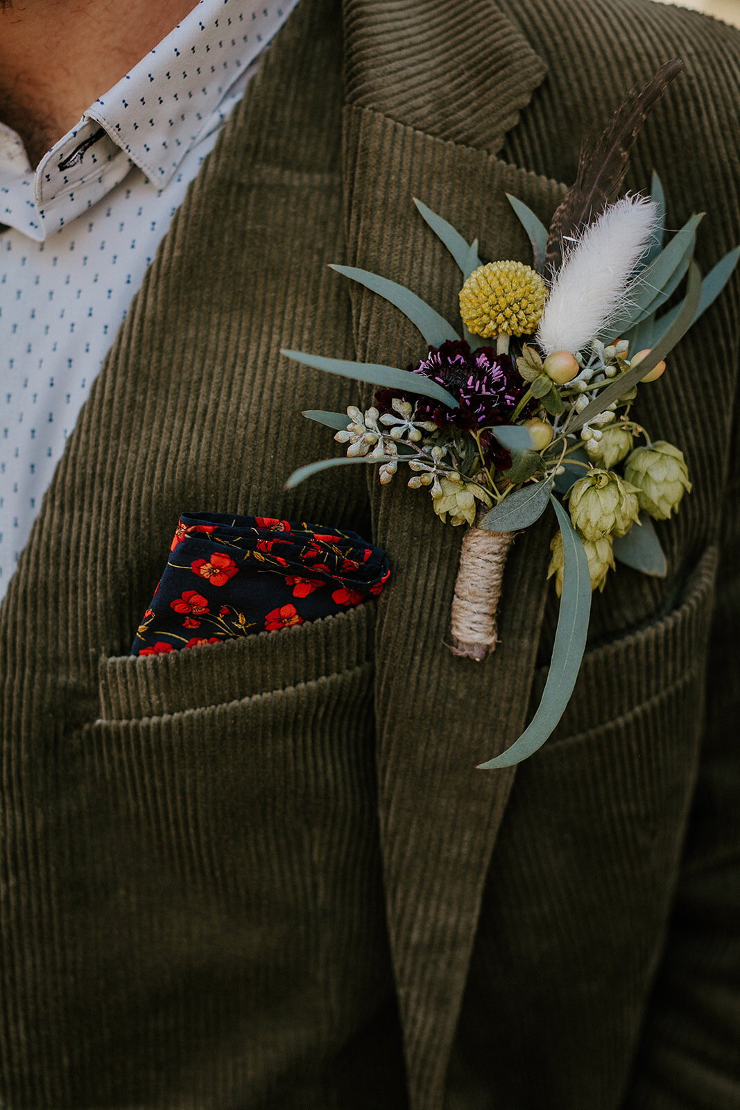 Boutonniere with hops, scabiosa, billy ball and bunny tail grass wrapped in twine on green jacket