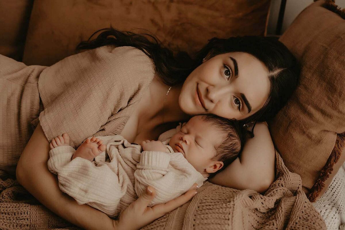 A mother holds her sleeping baby while she gazes at the camera in Rochester NY