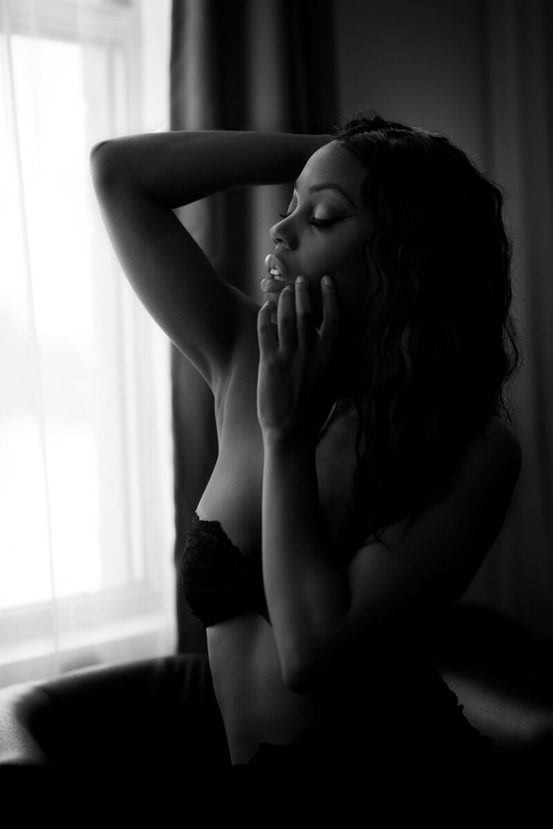 a black and white image in a denver boudoir studio of a black woman with long hair. She is wearing a strapless bra and running her and through her hair.