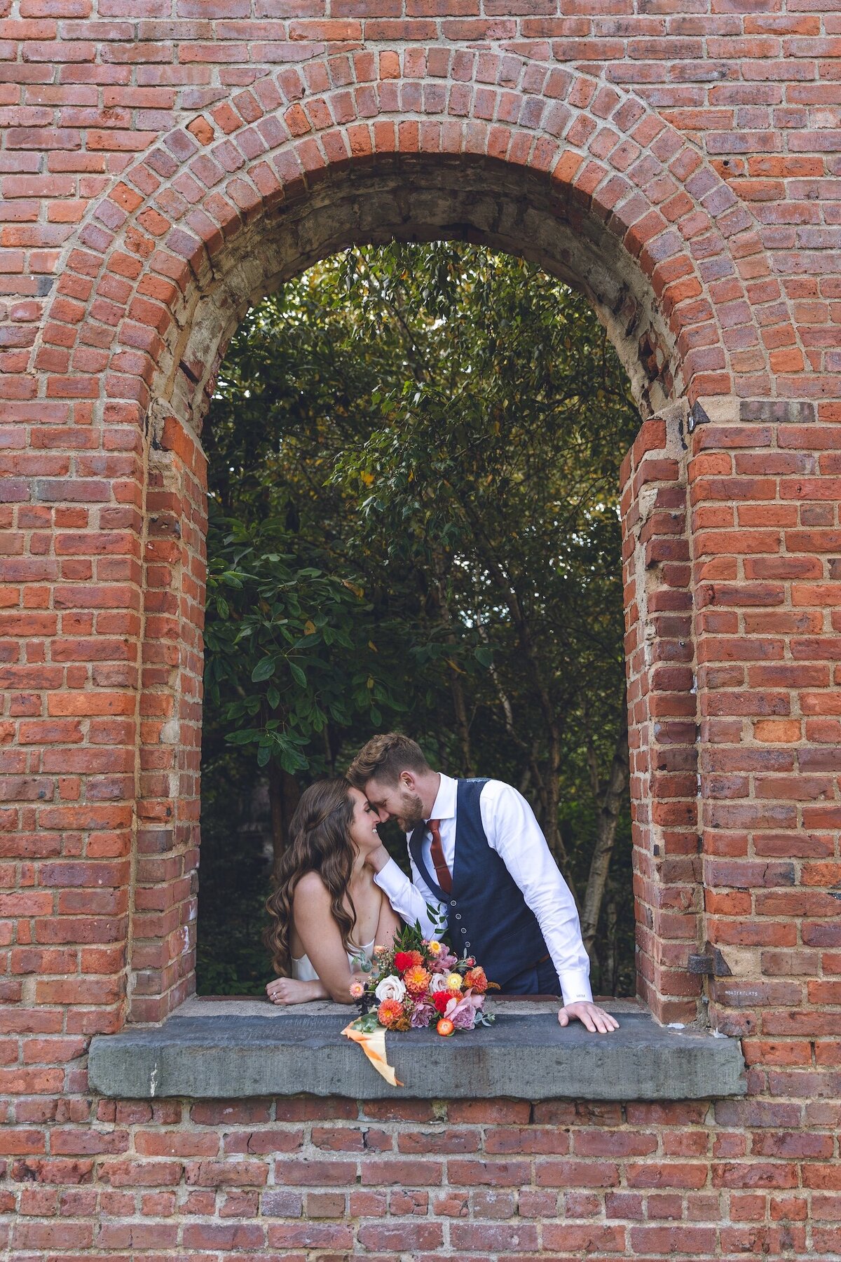 Bride and groom kissing through a brick arch in DUMBO