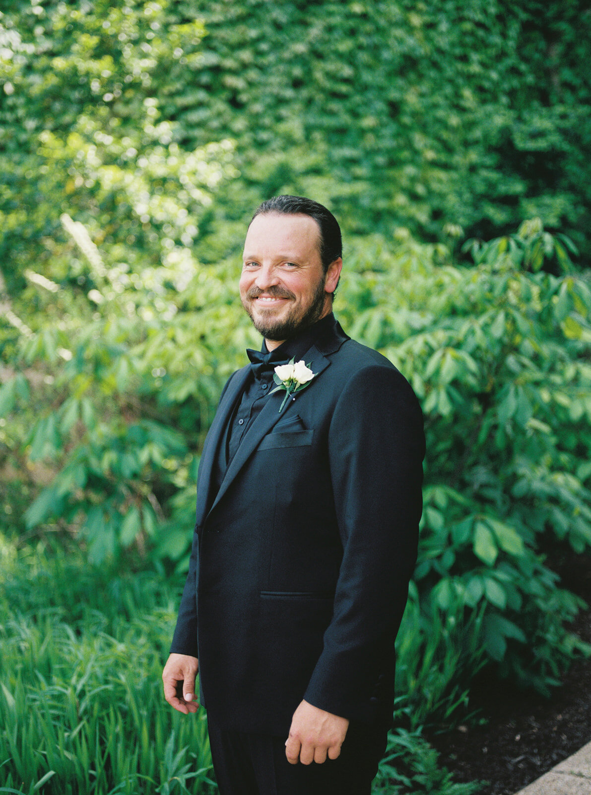 Groom dressed in all black smiles as he smiles towards the camera