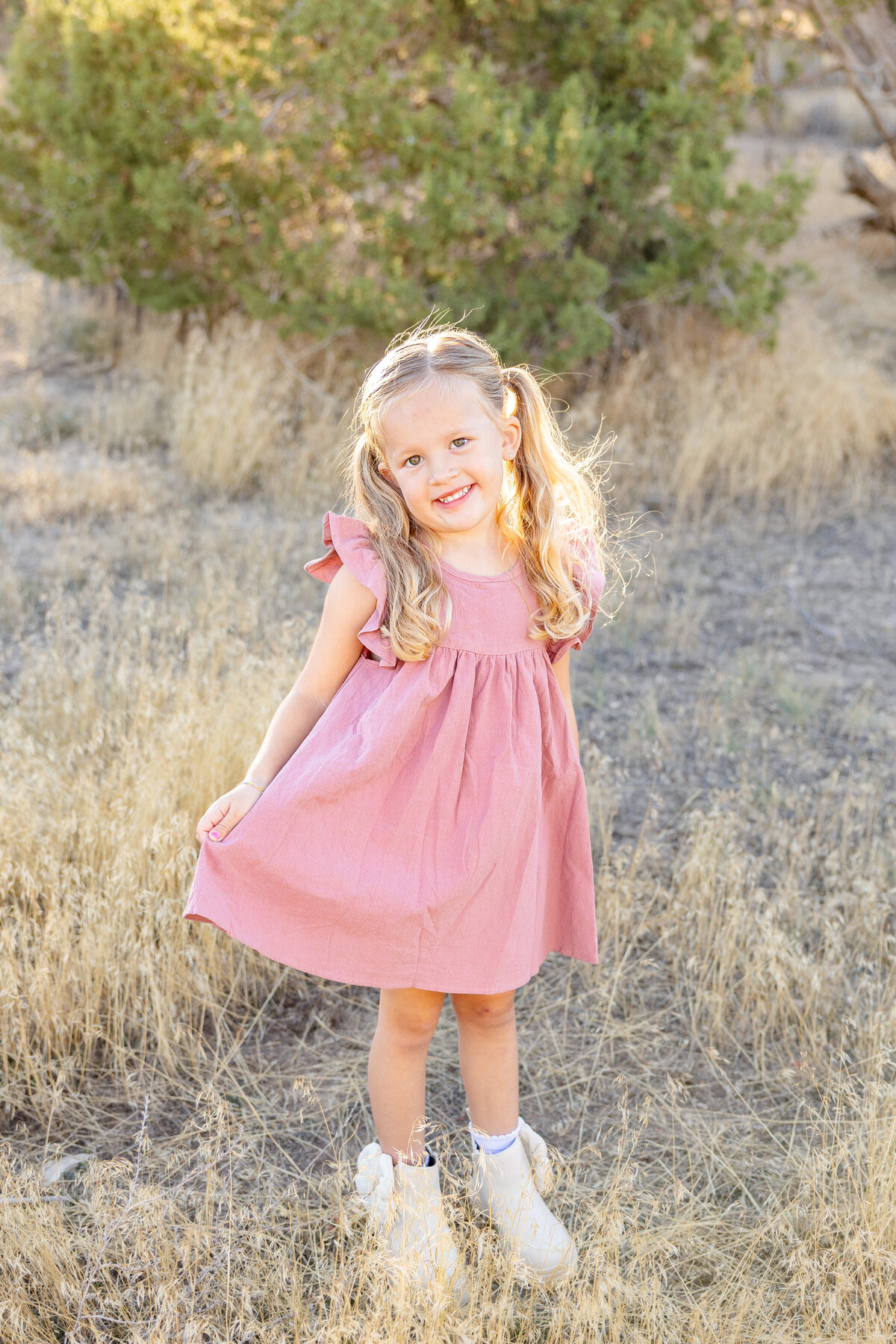A little blonde-haired girl twirls around in a pink dress, her expression full of joy.