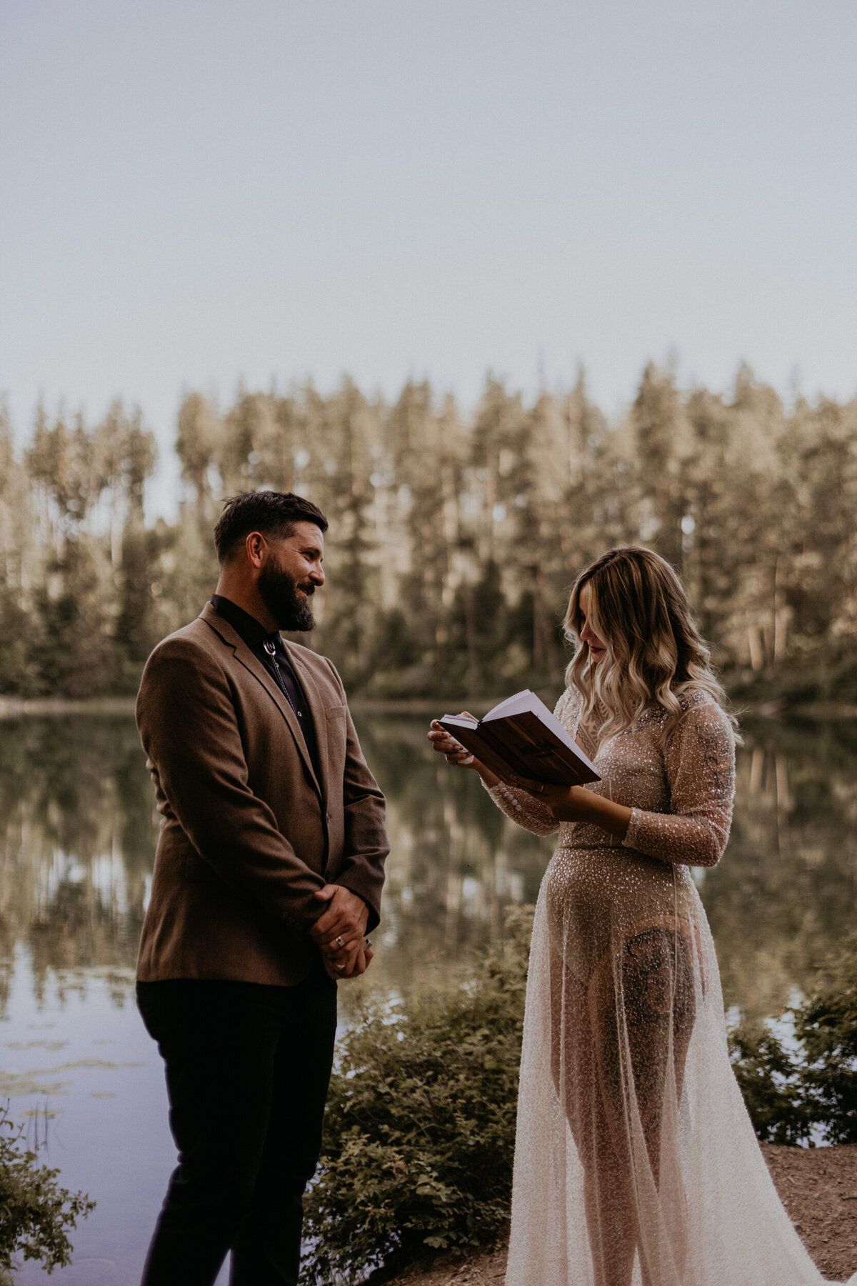bride and groom reading vows to each other in front of a lake