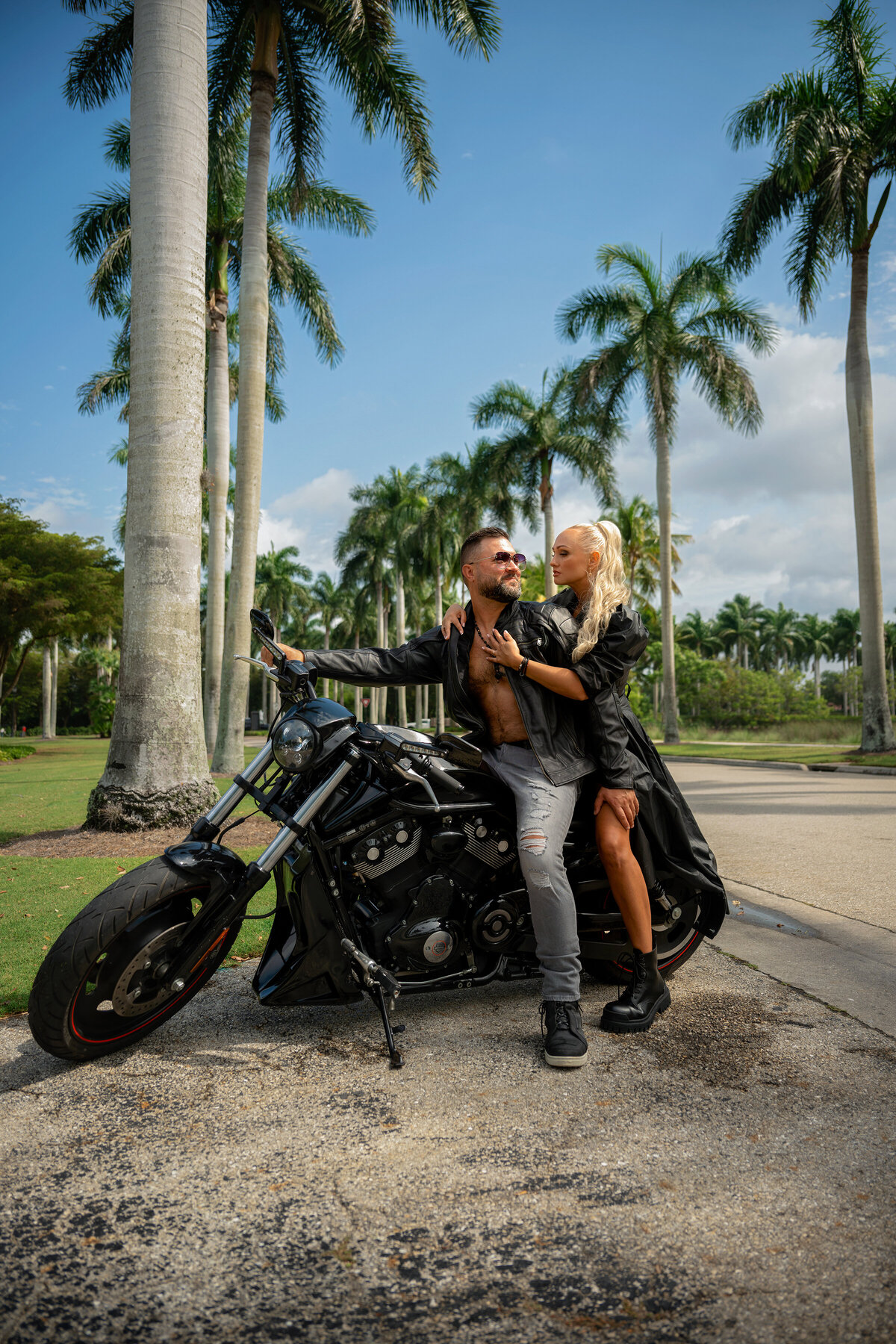 Engaged couple dressed in leather sitting on motorcycle in Naples Florida surrounded by palm trees