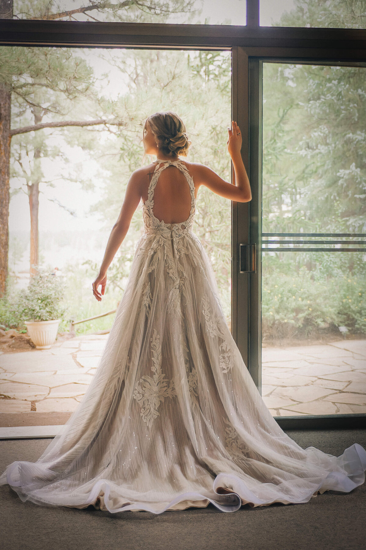 Bride in her wedding gown looking out a doorway into nature