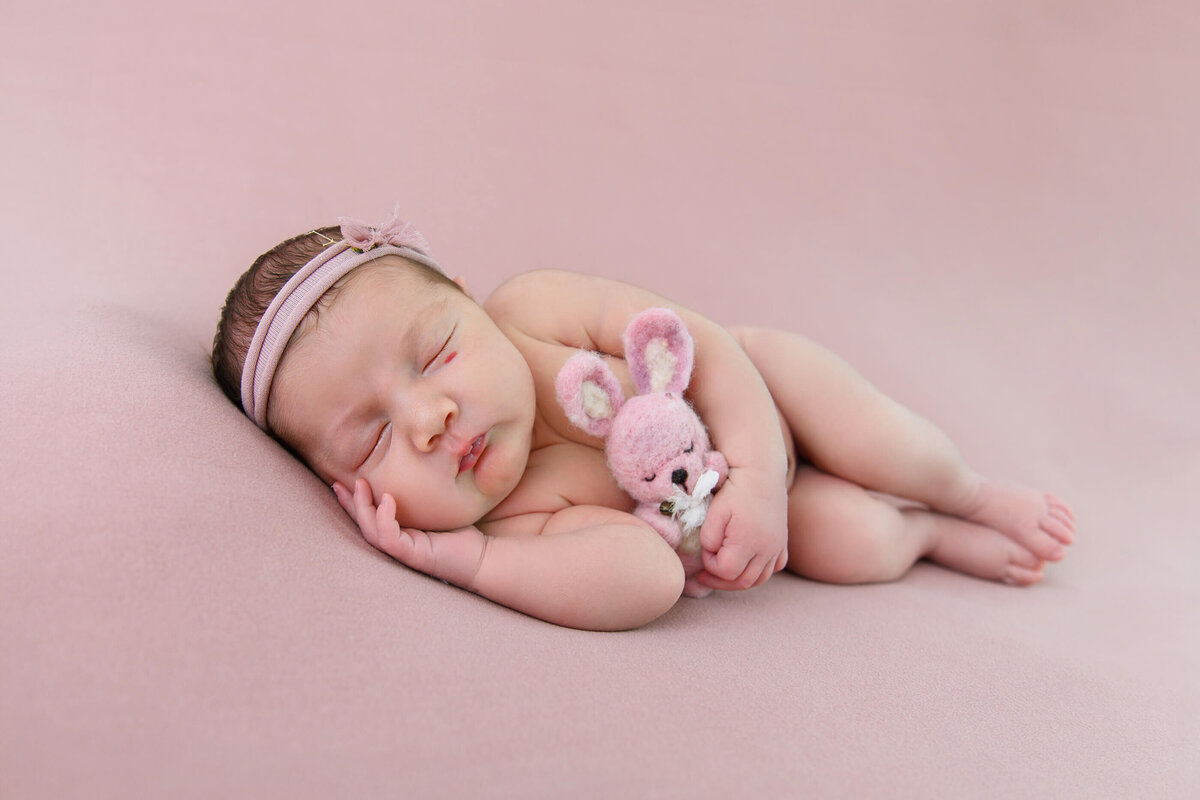 newborn girl side-laying on a pink background for her newborn photography session.