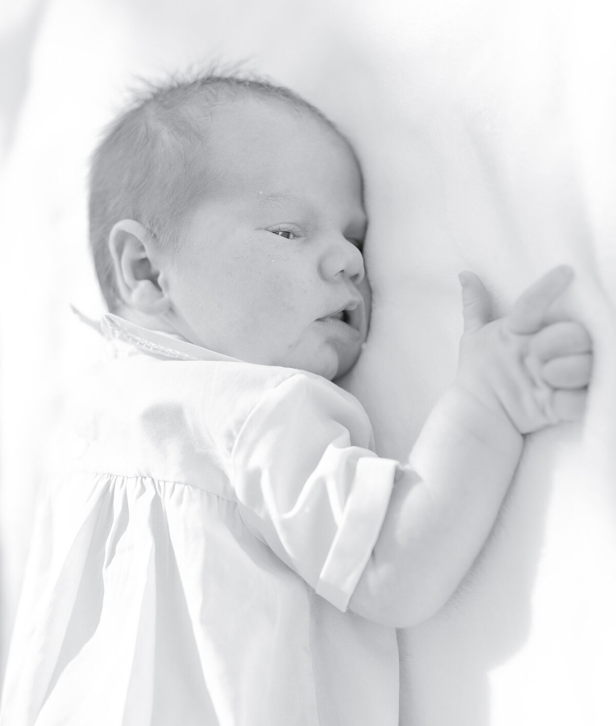  Newborn baby in white outfit, soft natural light, Birmingham newborn photographer – A peaceful newborn lying on a white blanket, gazing with curiosity, dressed in a delicate heirloom outfit.