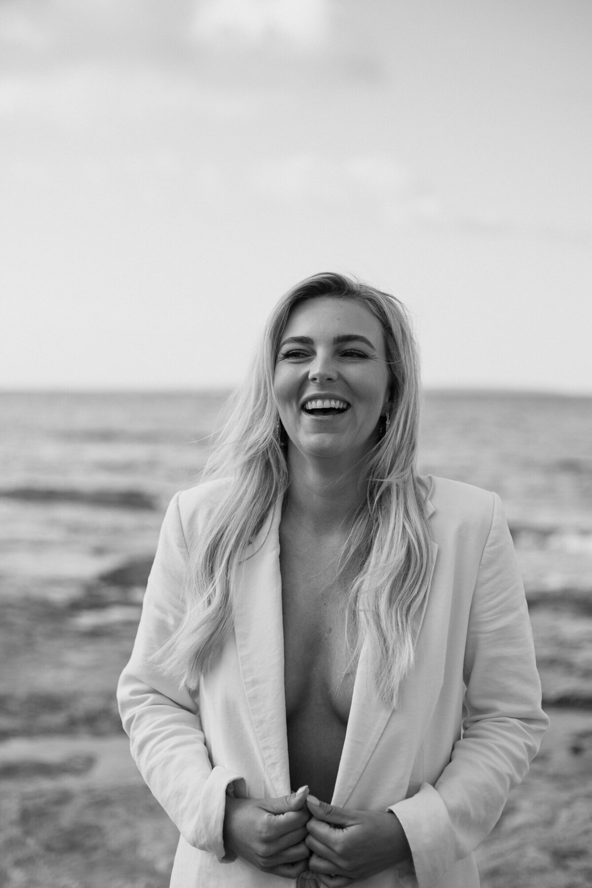 A woman is laughing while standing in front of the sea for personal branding photography on Ibiza