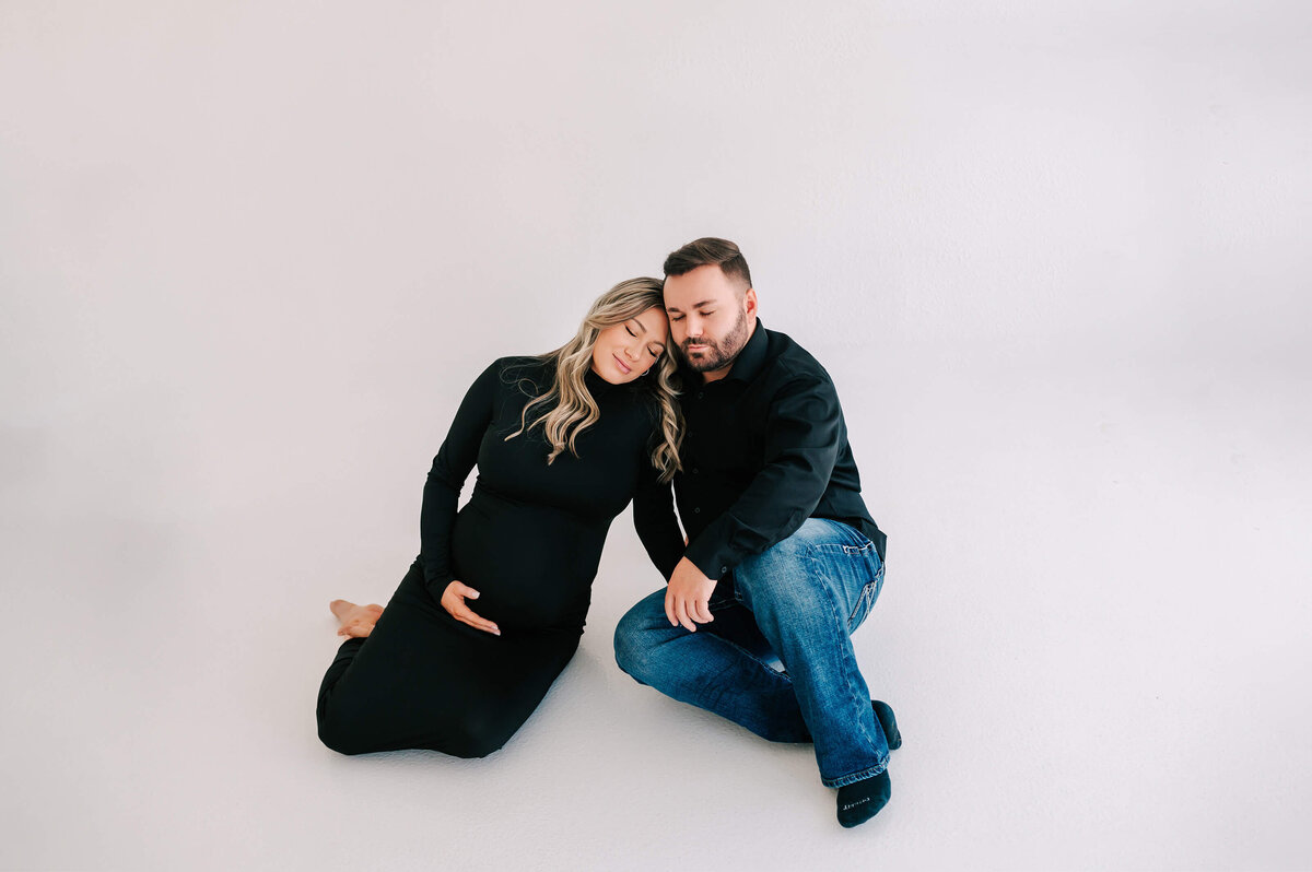 Branson Mo maternity photographer captures pregnant couple sitting on white floor cuddling