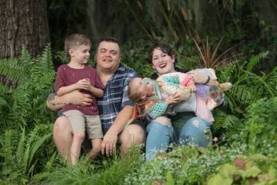 Happy family of four sitting together in lush fern garden during professional outdoor family photography session in St Augustine FL