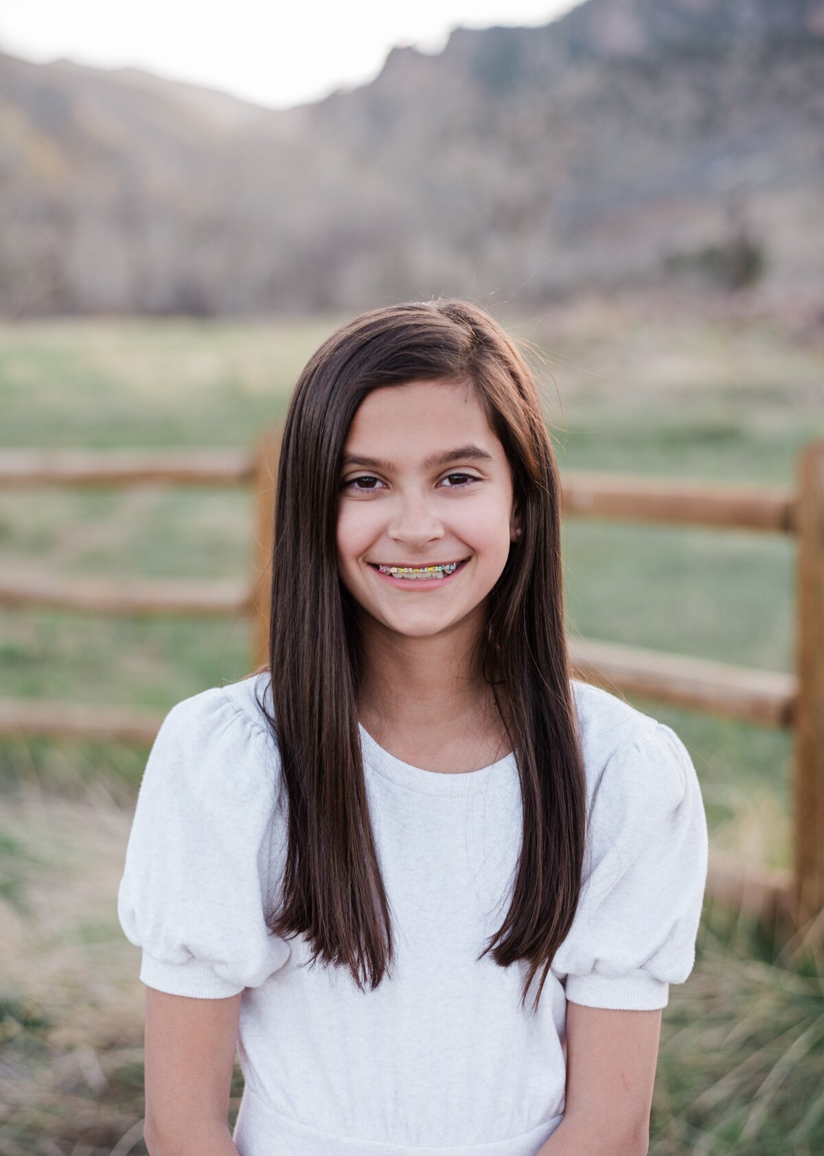 A young girl in a white top smiles at the camera with boulder flat irons behind her