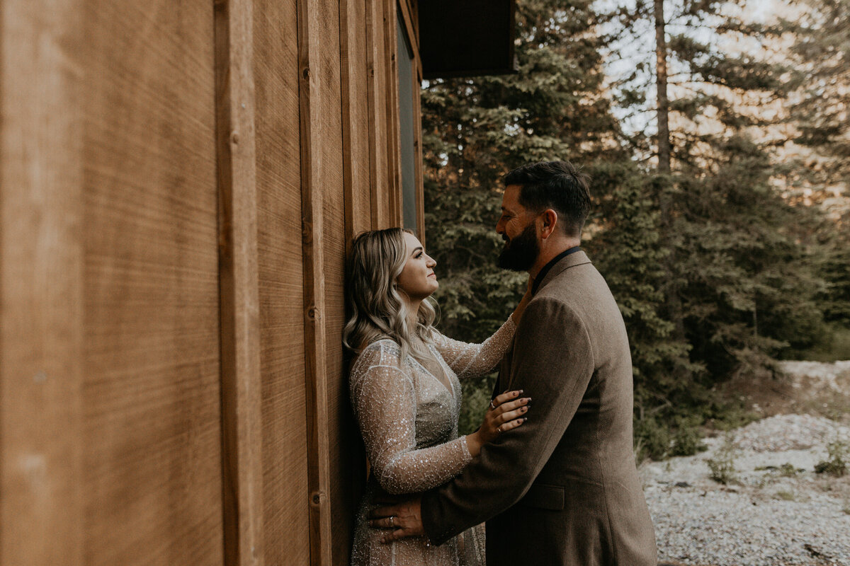 newlyweds standing against a cabin in their wedding attire