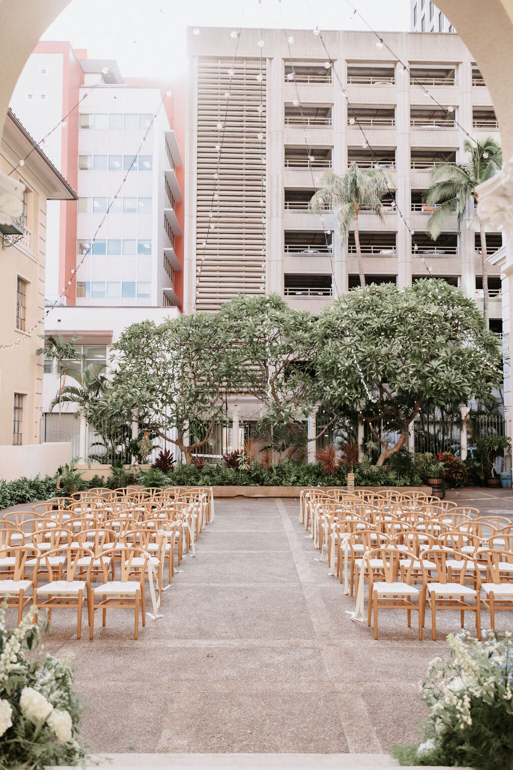 tall buildings with trees in front, and ceremony wedding set up wishbone chairs