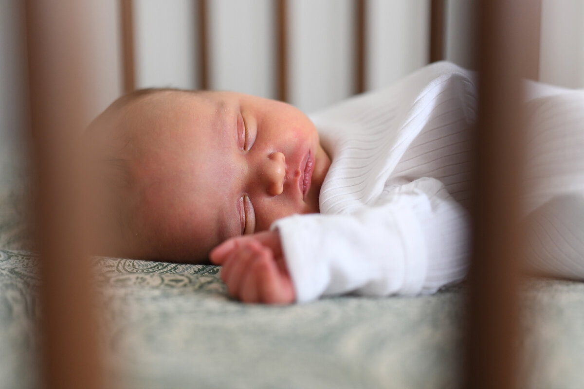 A serene newborn portrait capturing the gentle beauty of a sleeping baby in their crib. Soft natural light and cozy details make this in-home lifestyle newborn session in Connecticut timeless and heartfelt.