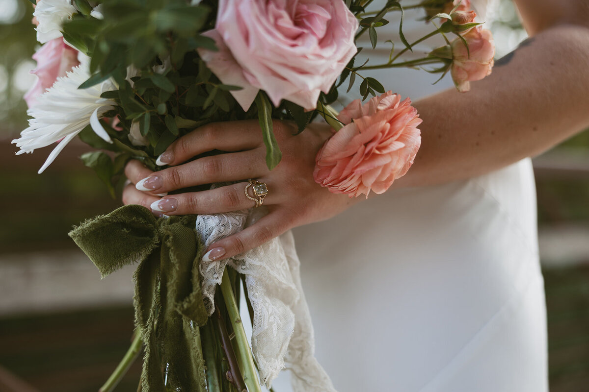 A bride in Overland Park, KS, holding her bouquet with one hand while showcasing her wedding ring with the other, capturing the elegance and beauty of her special day.