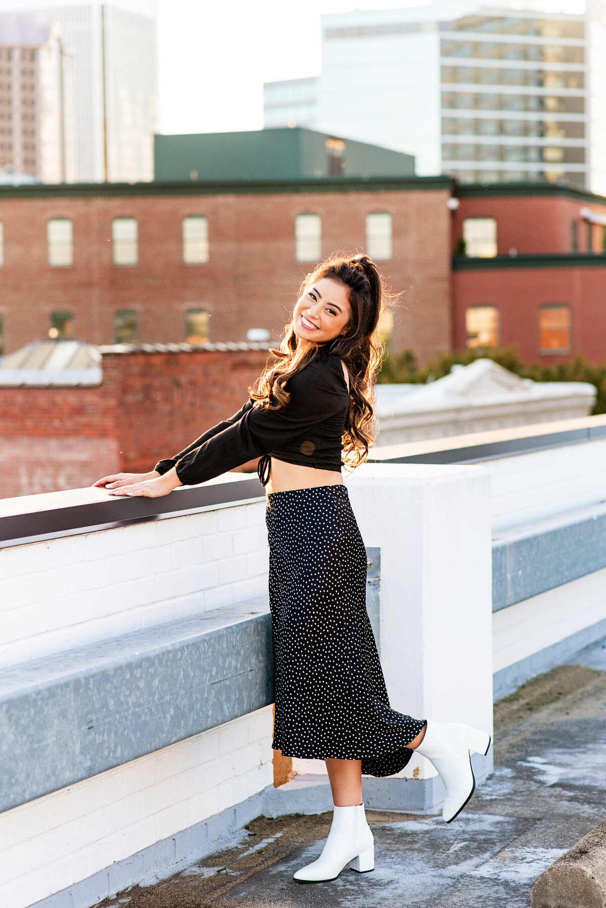 Senior girl poses with one foot up on rooftop at sunset.