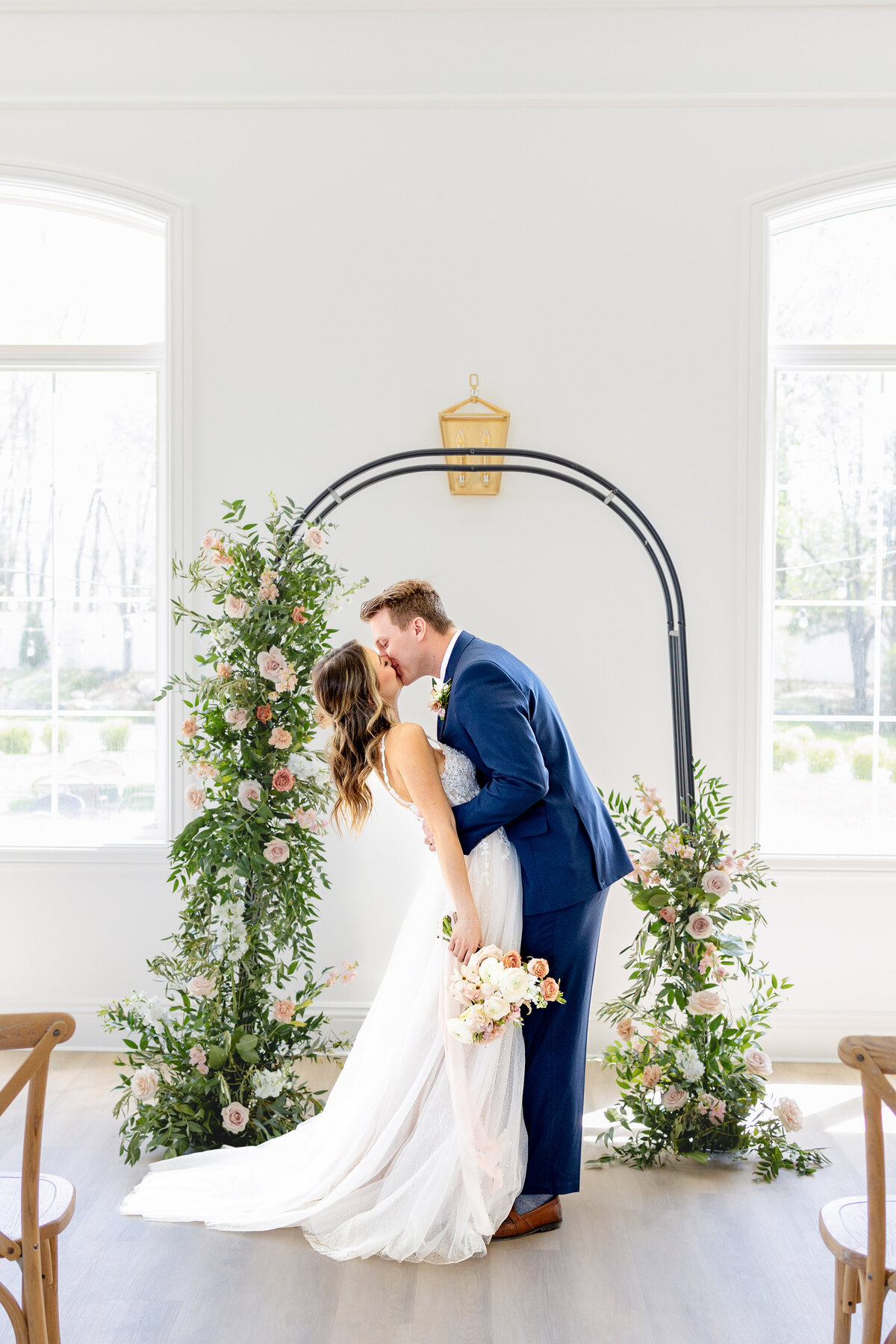 Groom passionately kisses his new bride for the first time under their arch with beautiful florals on it.