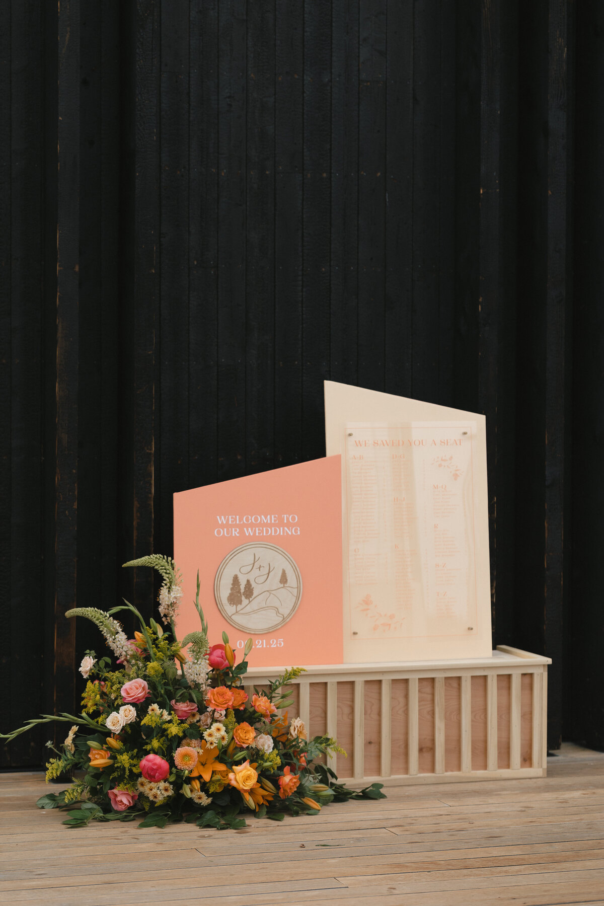 Seating chart and wedding welcome sign with coral and peach accents amongst natural wood and florals representing full service and design by Life in Letters