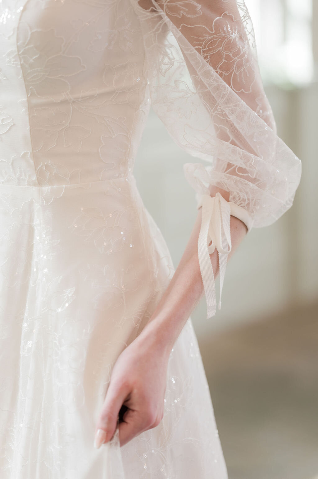 Close-up of the sparkly floral lace fabric and sleeve bow details on the Gene wedding dress style.